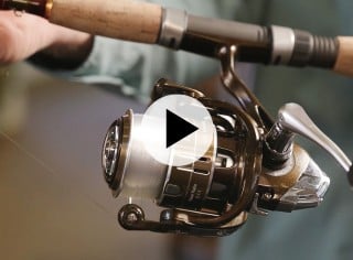 Close-up of a person holding a fishing rod with a spinning reel, ready for casting overlaid with a play video icon.