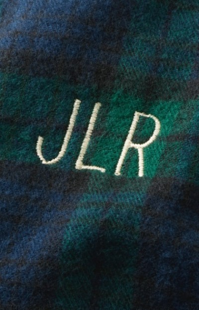 Close-up of blue and green plaid fabric with the initials “JLR” embroidered in white thread.