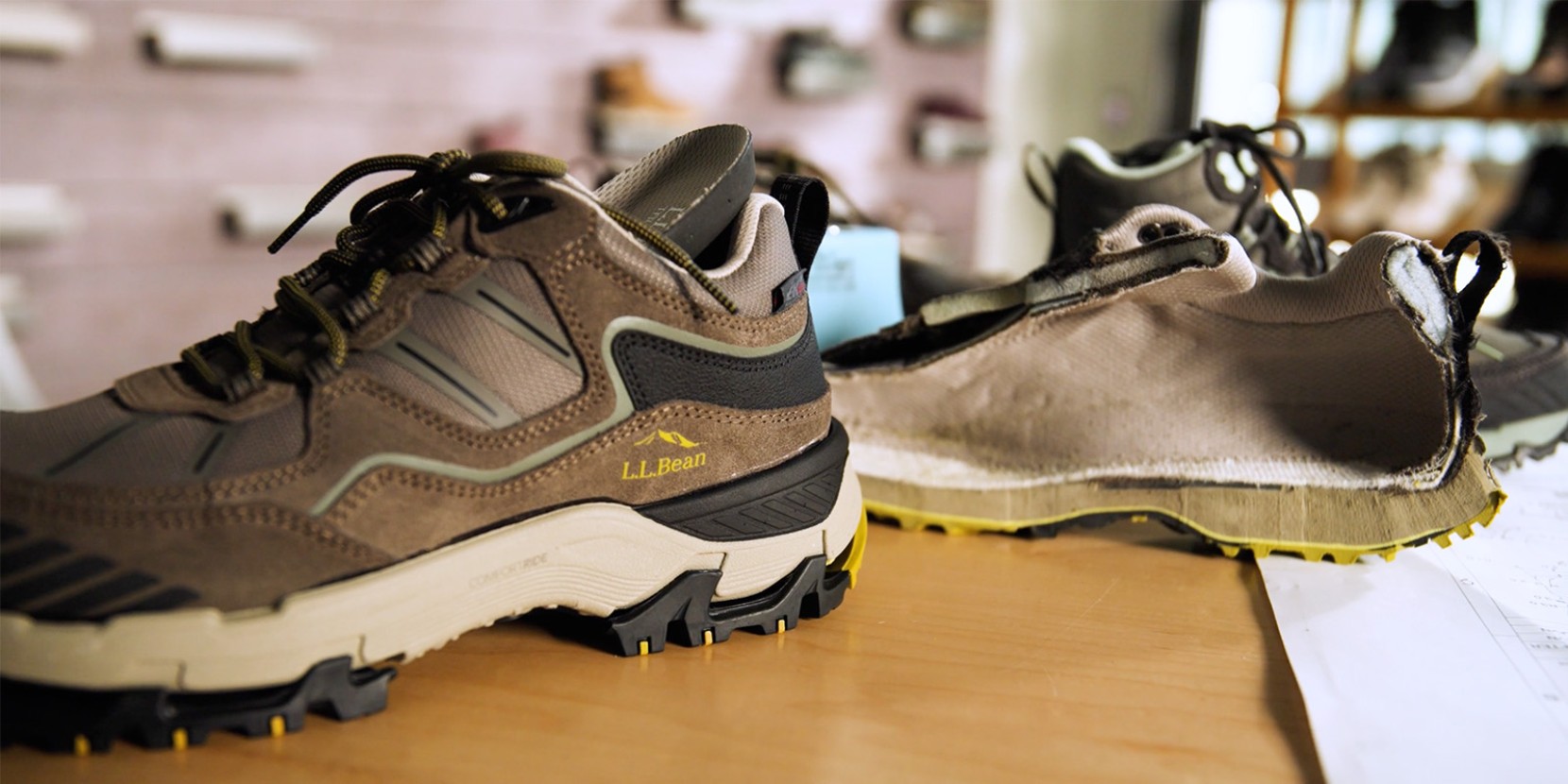 A hiking shoe cut in half lengthwise reveals its internal structure, displayed on a wooden table with papers nearby.