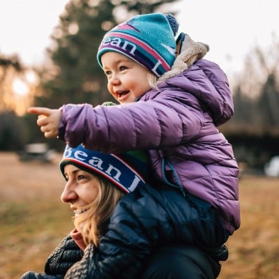 Mom carrying child on shoulders outside.