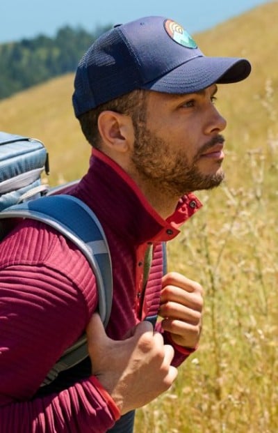 Hiker wearing a baseball cap and backpack looking across a grassy landscape.
