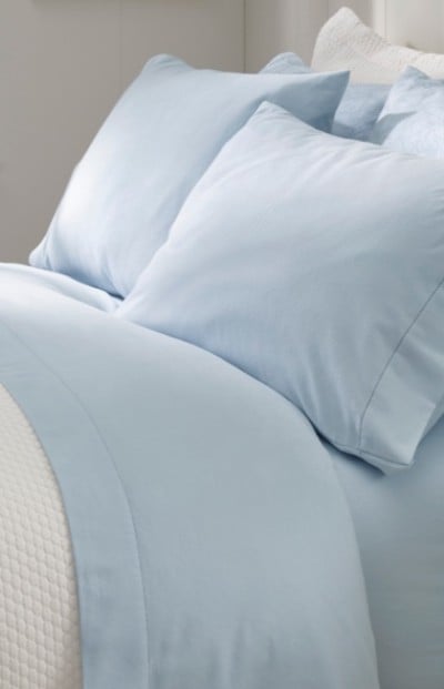 A neatly folded bed with matching light blue and white bedding and pillows.