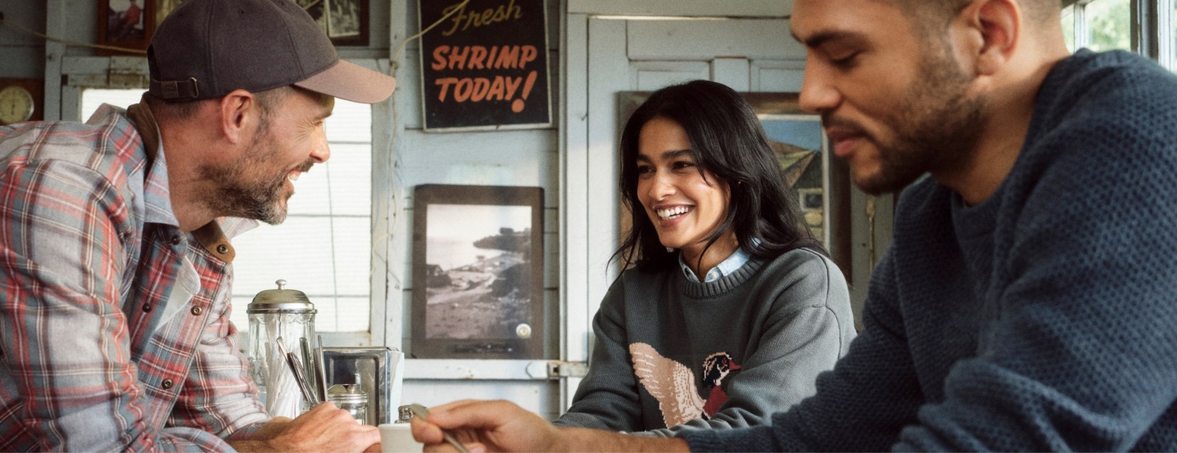 Three people sit together in a cozy seafood diner, sharing a conversation over drinks and a meal.