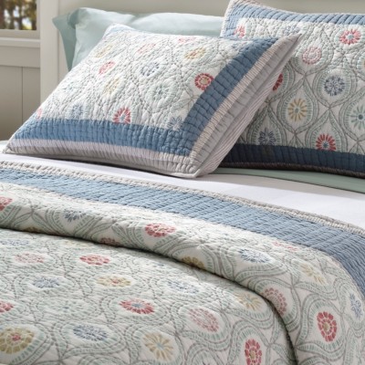 A neatly folded bed with a floral quilt and matching pillows.