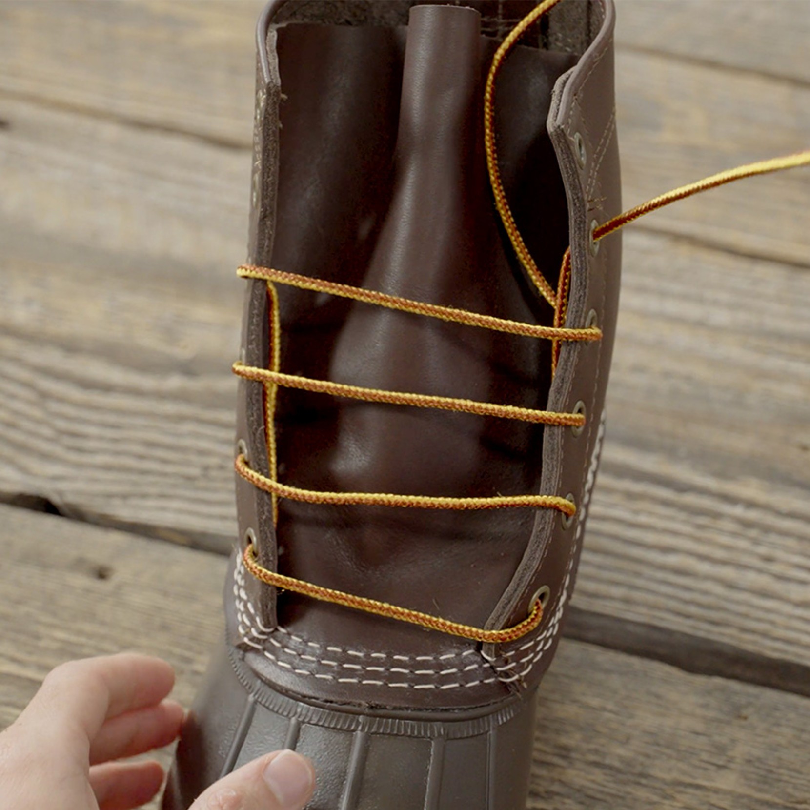 Brown boot with yellow laces partially threaded through metal eyelets.