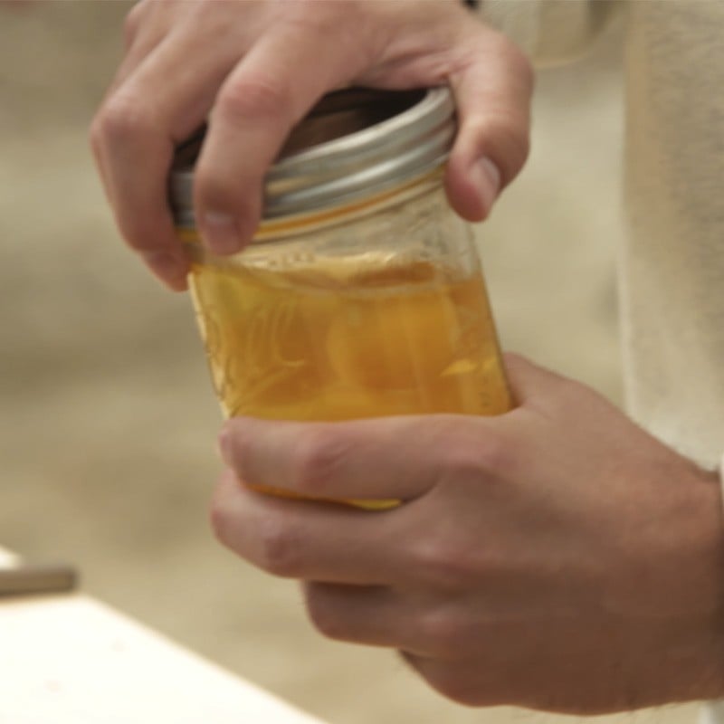 Hands holding a mason jar with cracked eggs.