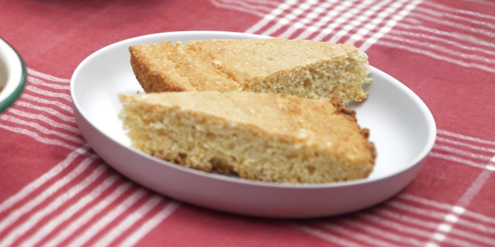 A plate of cornbread on a white plate, placed on a red and white striped cloth.