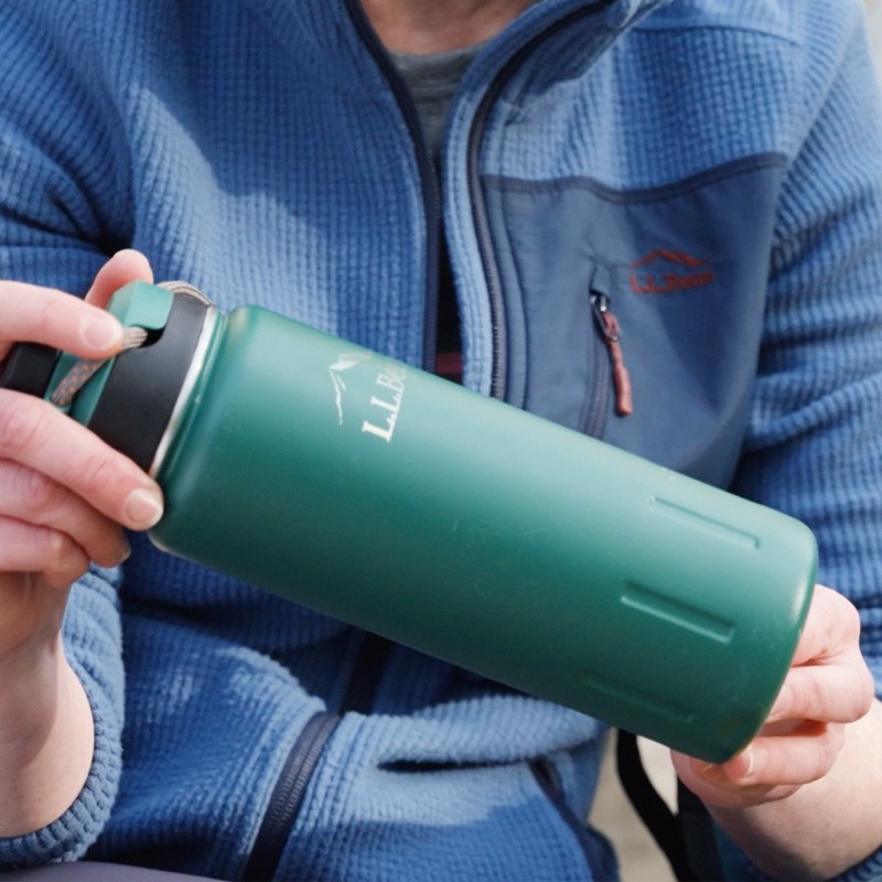 A close up of a person holding a green L L Bean water bottle.