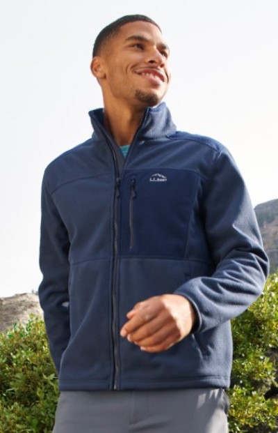 A man in navy full-zip fleece jacket with chest pocket and logo, worn over a blue shirt in an outdoor setting.