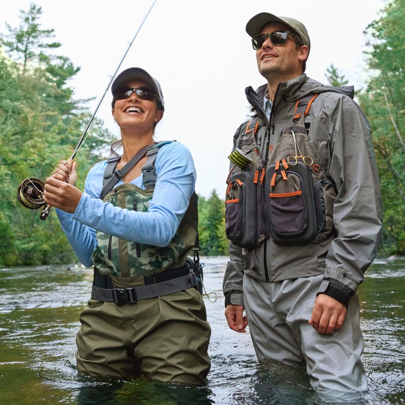 A man and woman in waders standing in a river fly-fishing.