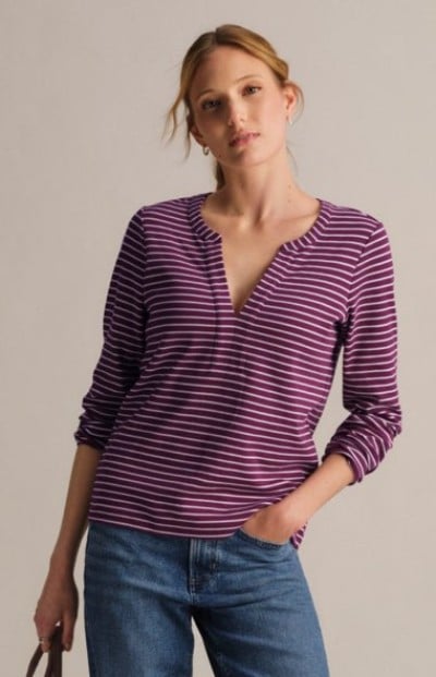 Person wearing a burgundy striped V-neck shirt and blue jeans against a neutral backdrop.