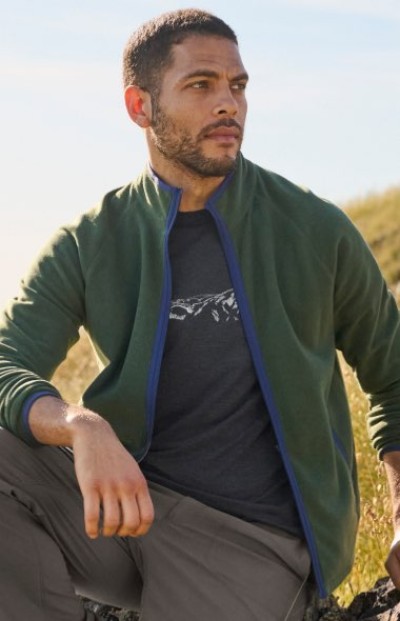 Person wearing a green fleece jacket seated outdoors with one arm resting on a raised knee.