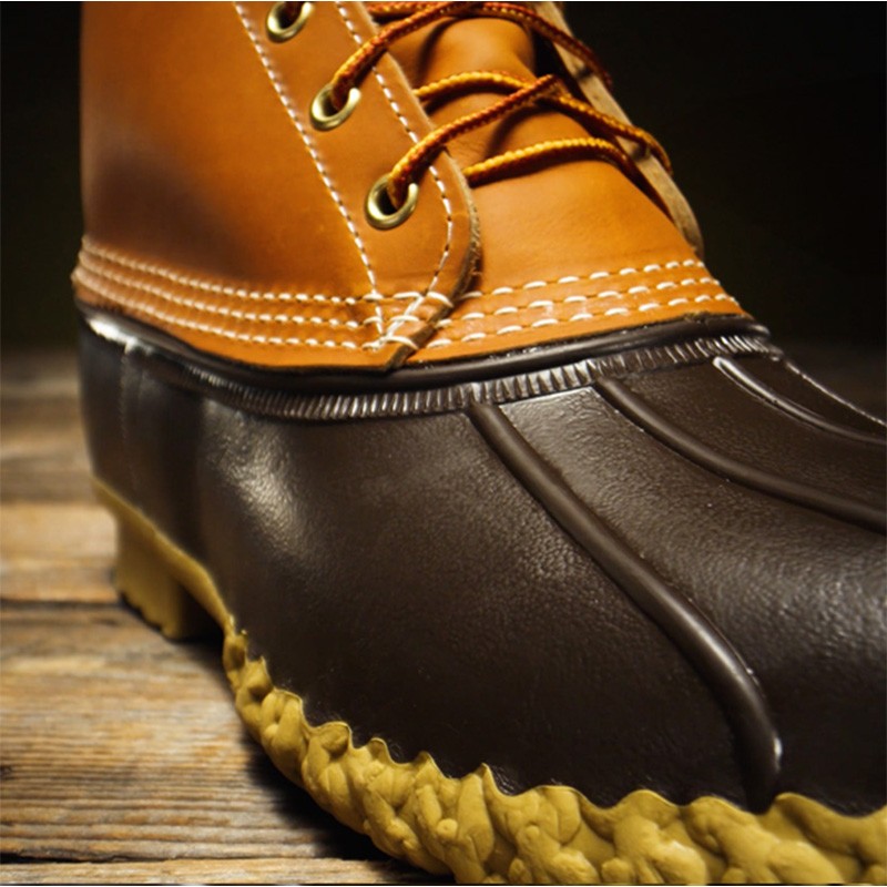 An L L Bean boot with yellow laces, detailed stitching, and a textured rubber sole on a wooden surface.