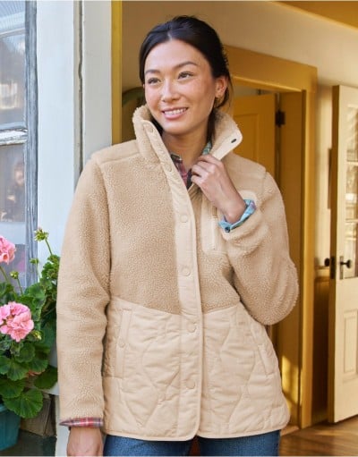 Person stands near a doorway wearing a tan fleece jacket with quilted details.
