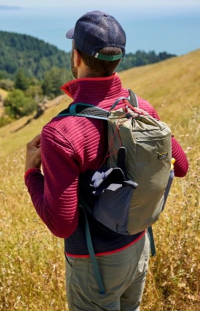 Hiker wearing a backpack while standing on a grassy hillside trail.