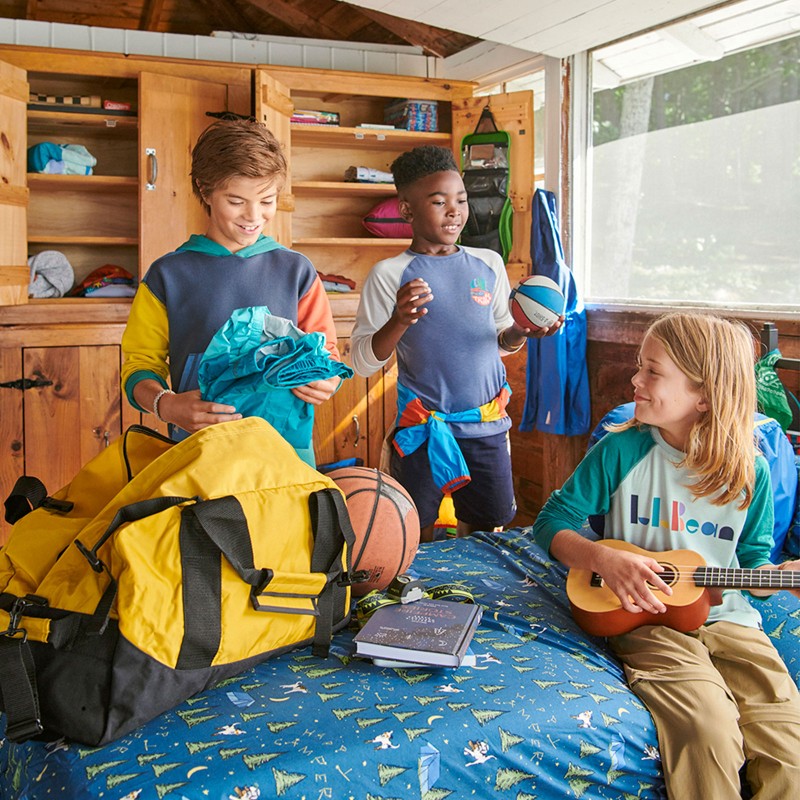 3 kids in a rustic cabin, one unpacking his duffle bag.