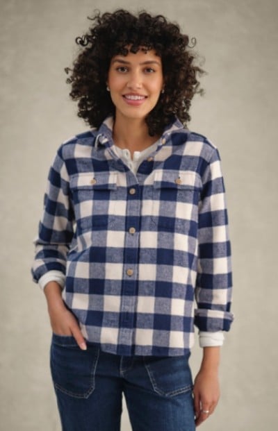 Woman in blue and white checkered shirt with rolled-up sleeves stands against plain background.