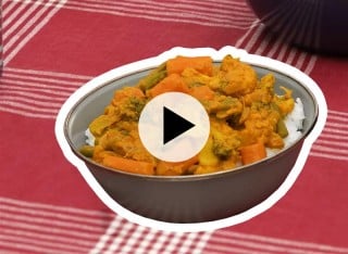A bowl of curried vegetables sitting on a red and white checkered tablecloth.