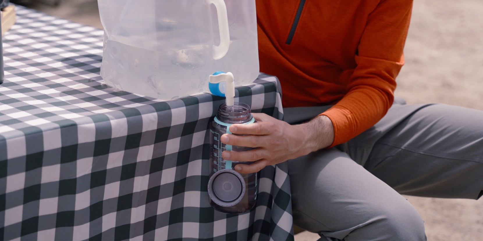 A person is refilling a water bottle from a large dispenser outdoors.