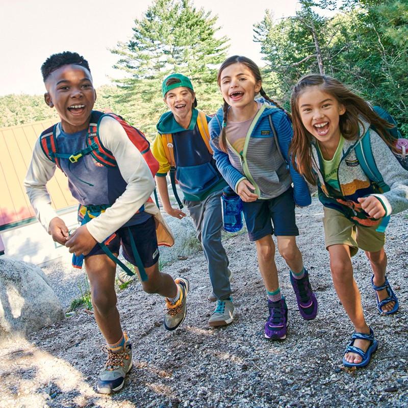 4 smiling kids outside wearing backpacks.