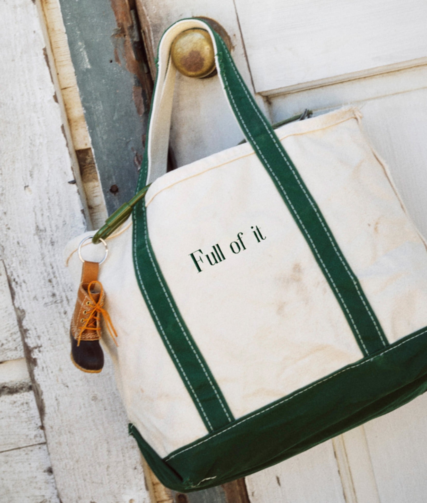 Canvas tote bag with green trim hangs from a weathered boathouse door.