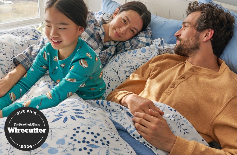 Parents and child in pajamas while lounging on a cozy bed with blue floral print.