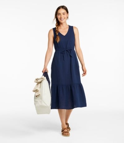 Person in navy sleeveless midi dress holding a tote bag, standing against a light background. 
