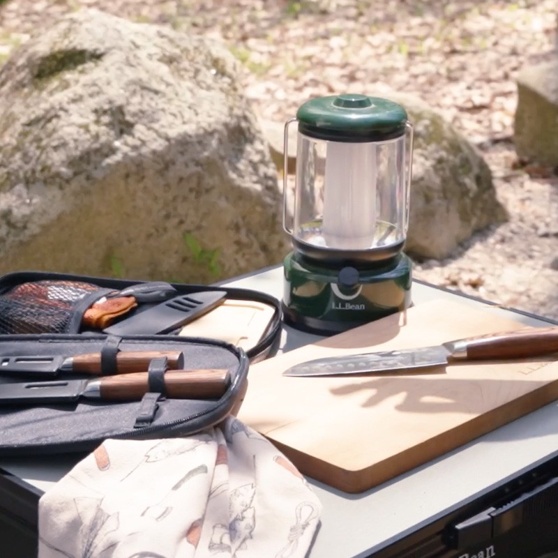 Outdoor camping gear on a table, including a lantern, cutting board, and utensil organizer.