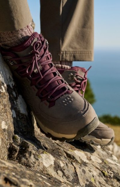 Rugged hiking boot with purple laces perched on a rocky outcrop.