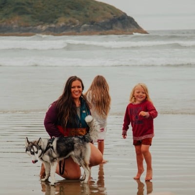 A woman with two young girls and a dog at the beach.