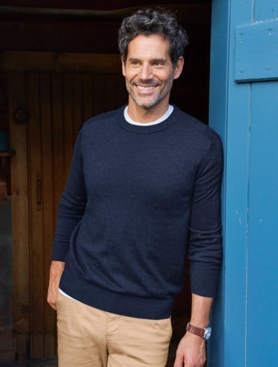 Man in a navy sweater stands in a wooden doorway outdoors. 