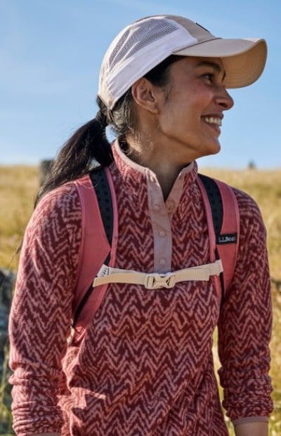 Hiker in a patterned pullover and cap wearing a backpack in a sunny landscape.