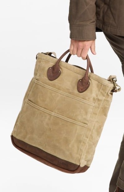 Hand carrying a tan canvas tote bag with brown leather handles.